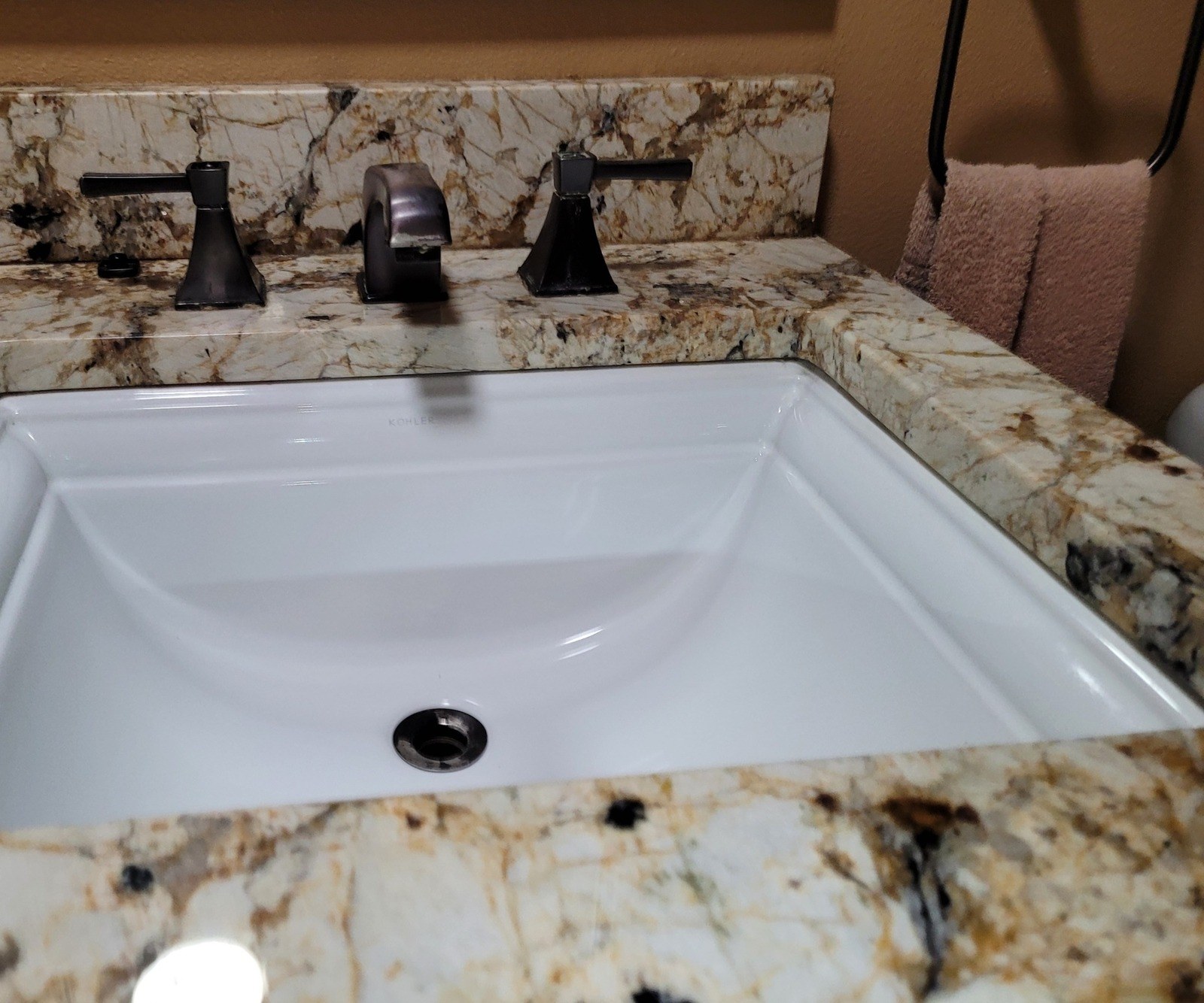 Oil-rubbed bronze two-handle widespread bathroom faucet on a granite vanity top above a white rectangular undermount sink, before replacement