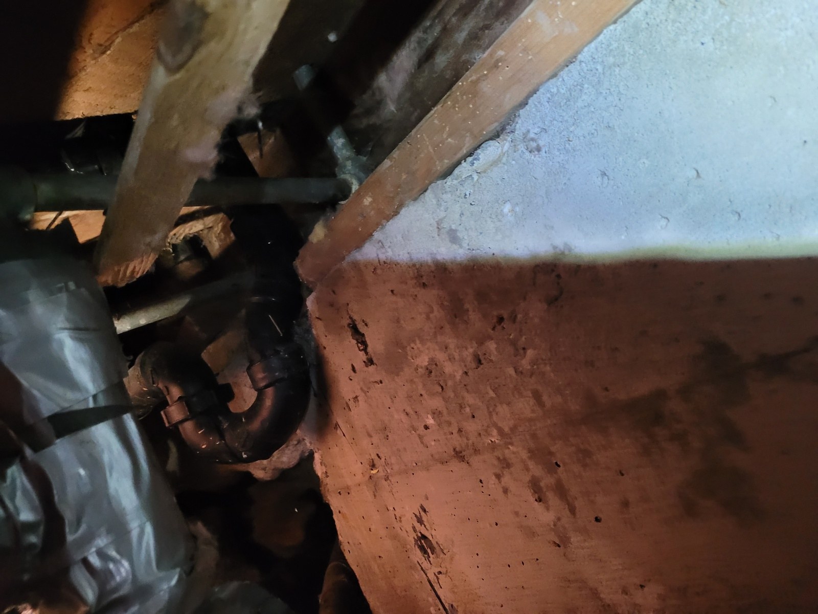New black ABS waste and overflow assembly connected under a bathtub in a dim crawlspace