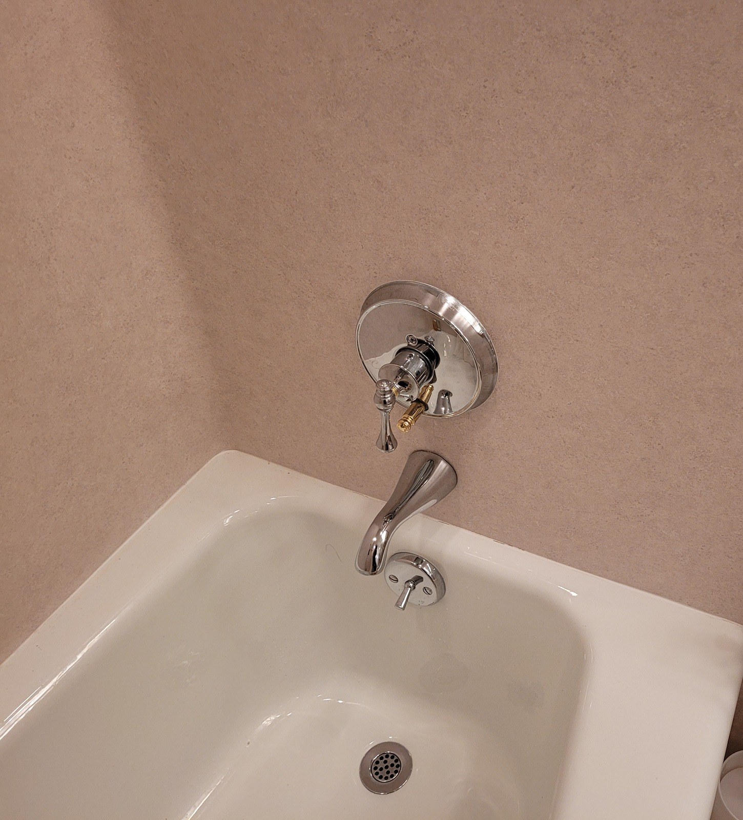 Chrome lever and round trim plate reinstalled on a Kohler tub and shower valve in a beige cultured-marble surround, with a brass stem showing below the lever, above a white tub and chrome spout
