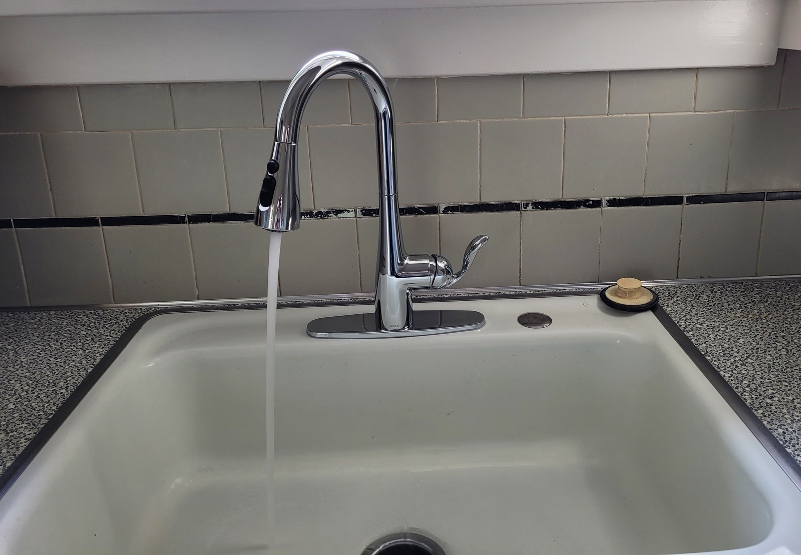 Chrome Moen single-handle pulldown kitchen faucet running into a pale green enameled sink below a gray tile backsplash