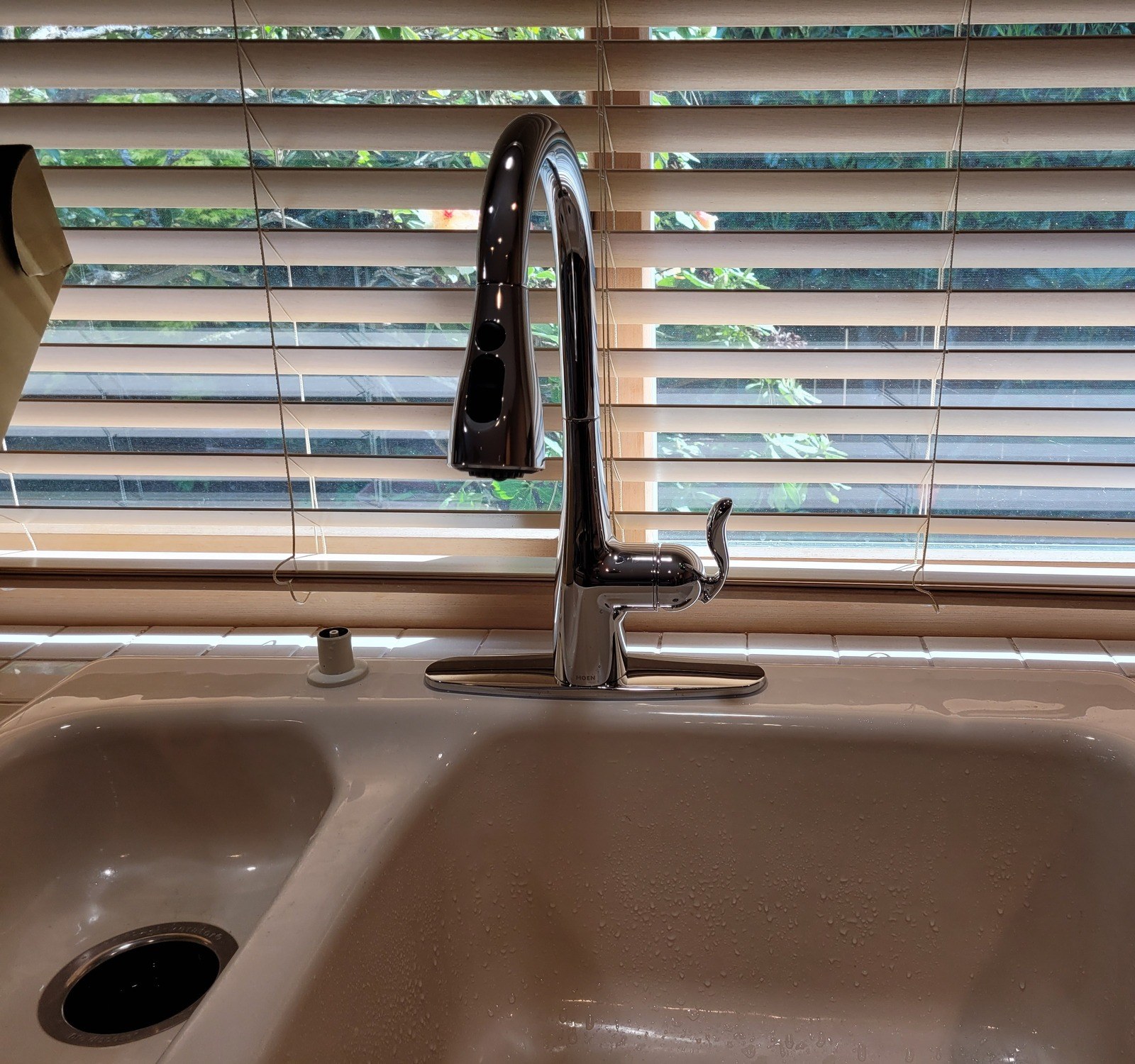 Chrome Moen Arbor single-handle pulldown kitchen faucet on an almond double sink, in front of half-open window blinds