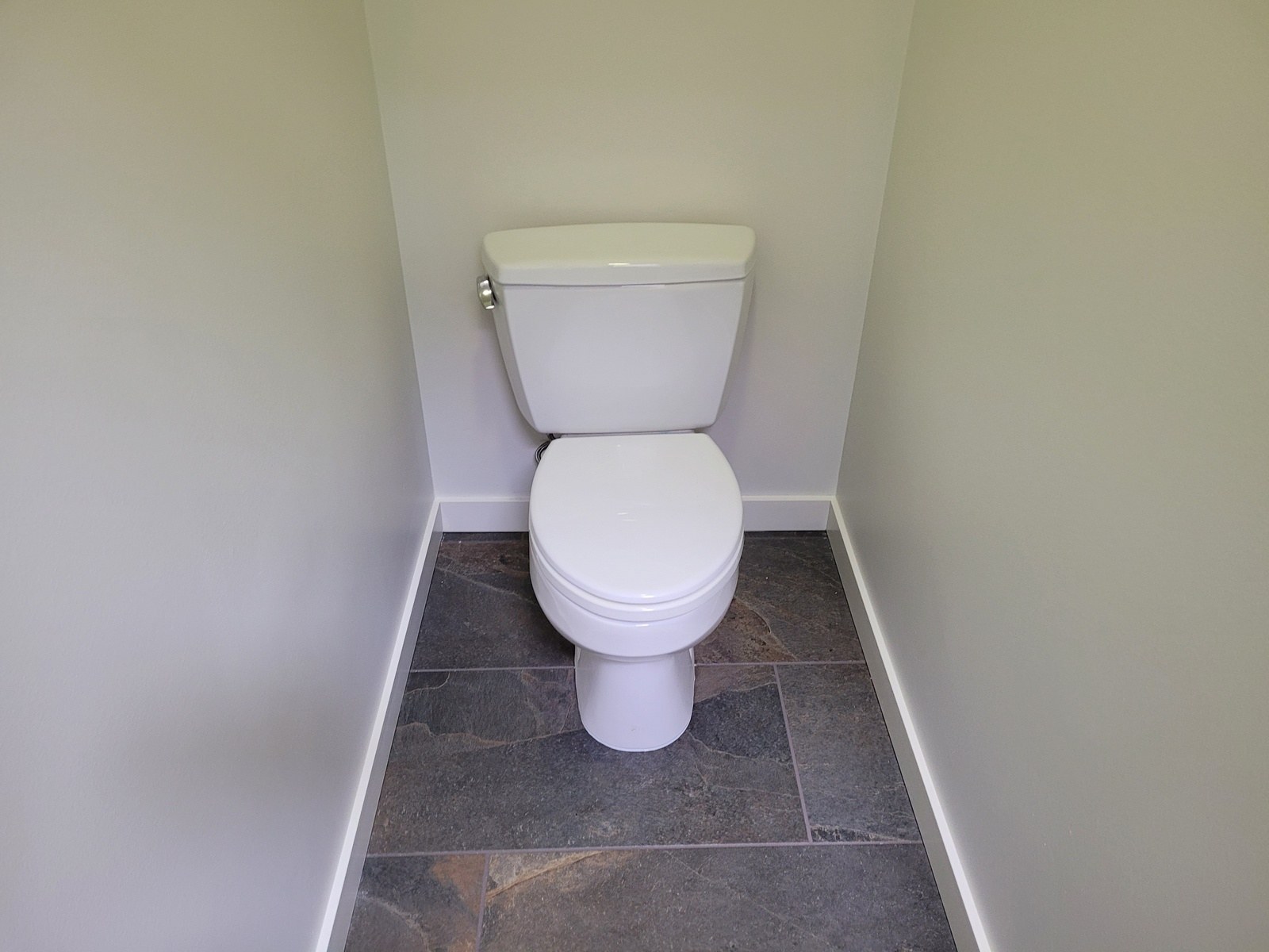 A reinstalled toilet in a freshly finished water closet with new tile floor and clean baseboards