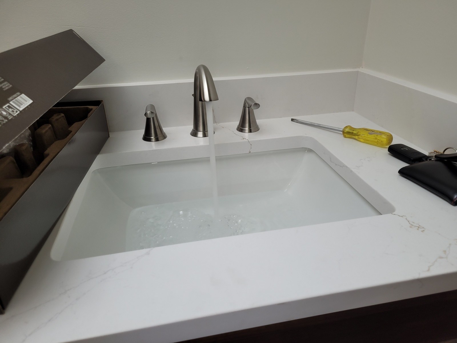 New widespread bathroom faucet running water into an undermount sink in a fresh quartz vanity top