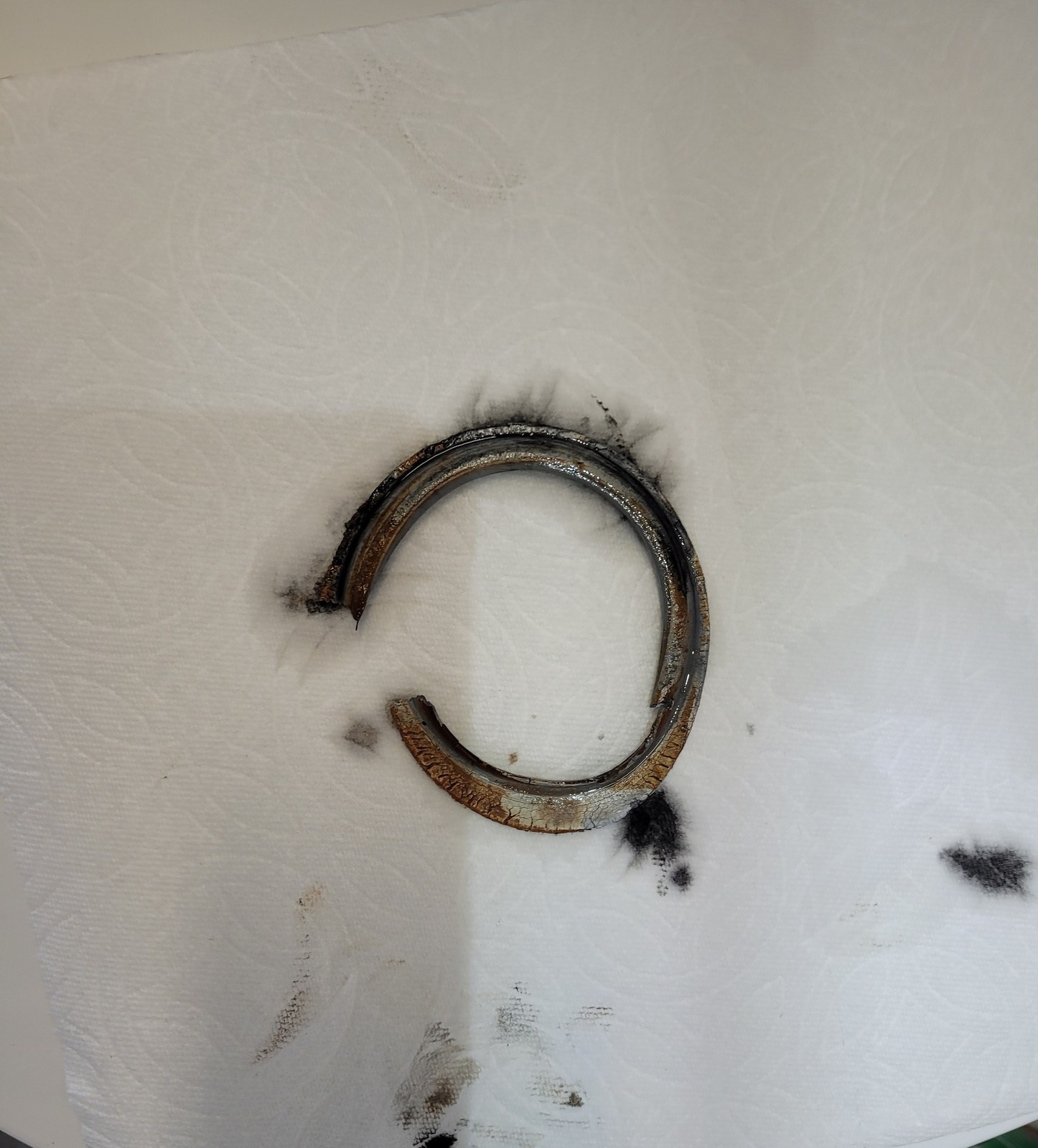 An old rubber toilet flush-valve seal, split and crusted with rust, lying on a paper towel