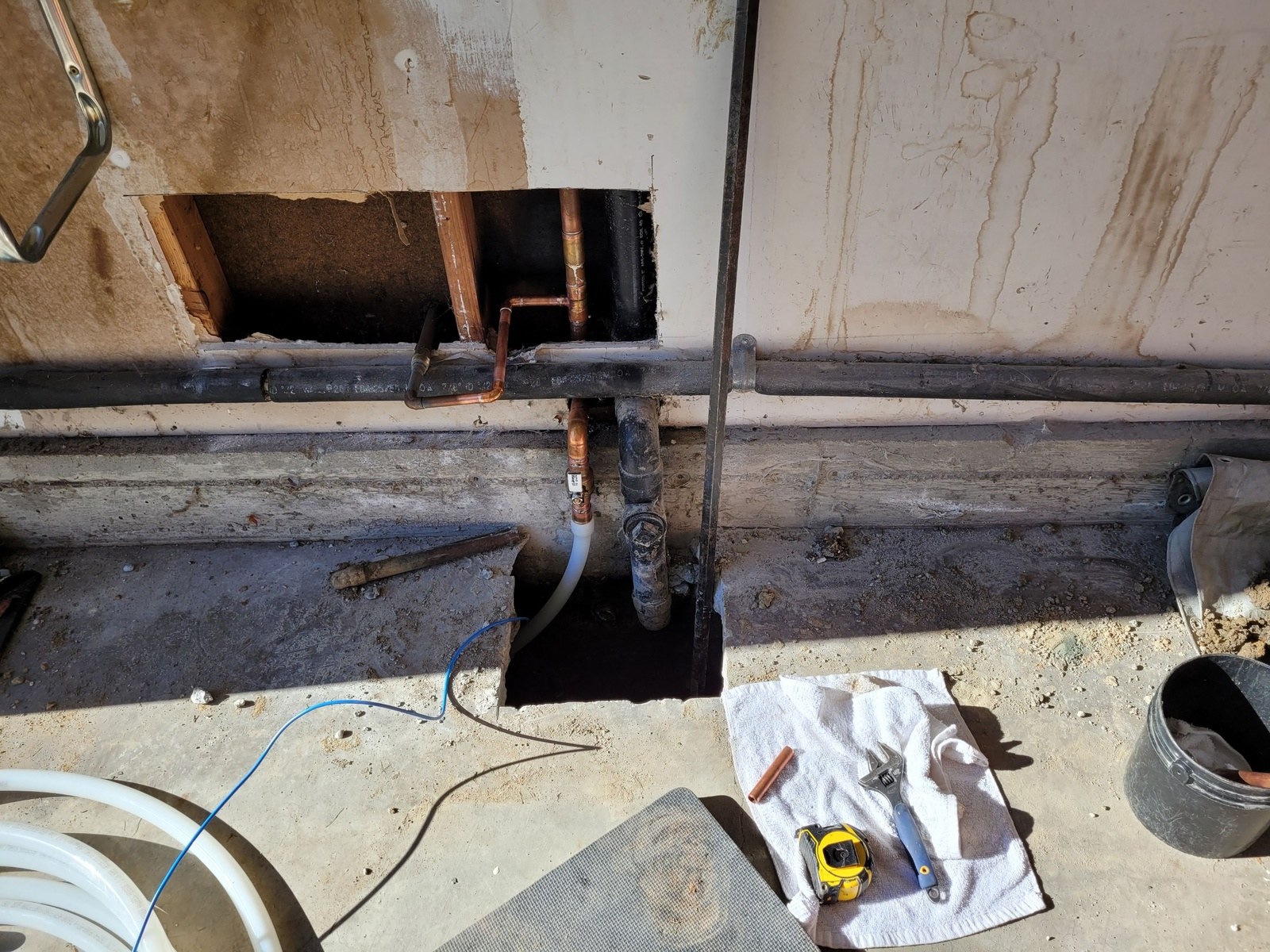 Garage-side tie-in of a new water service β white service line rising through a neat slab opening with blue tracer wire, connected to copper with a new ball valve
